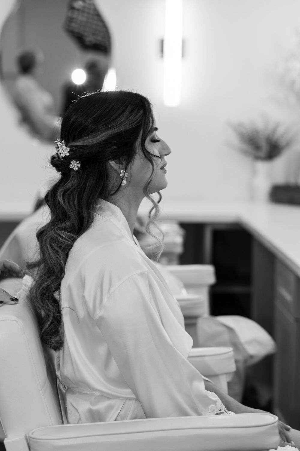 A bride in a white robe sits while getting ready on her wedding day.