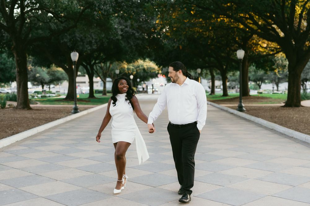 A couple walks hand in hand along a tree-lined path during a romantic outdoor photoshoot.