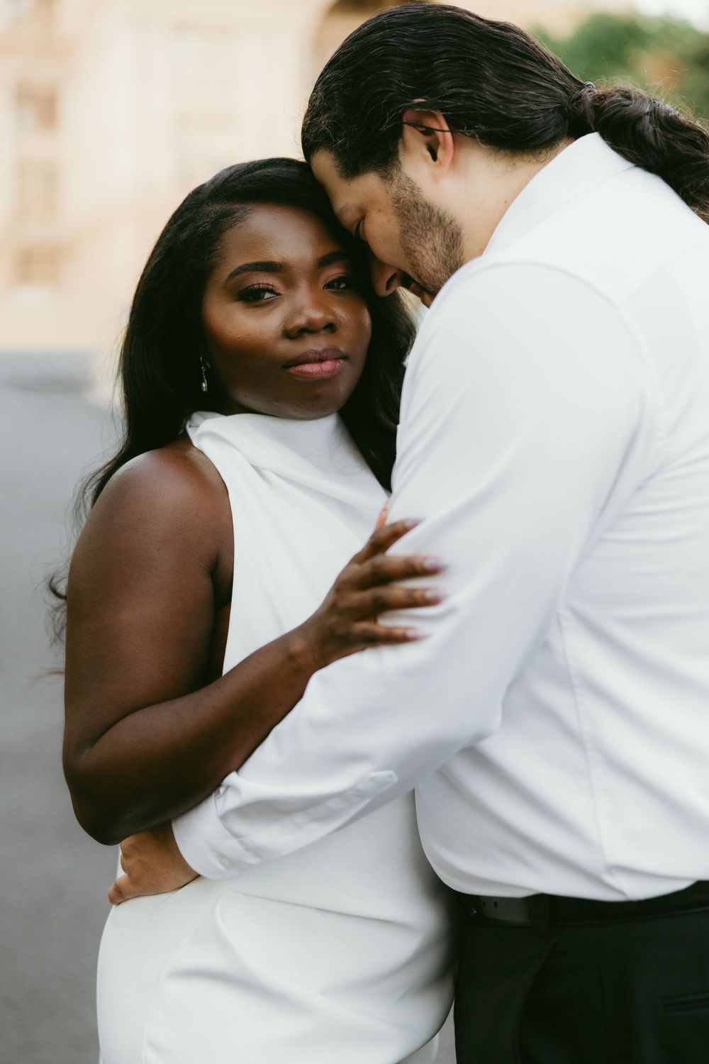A couple in contrasting black and white outfits share an intimate embrace during an outdoor photoshoot.