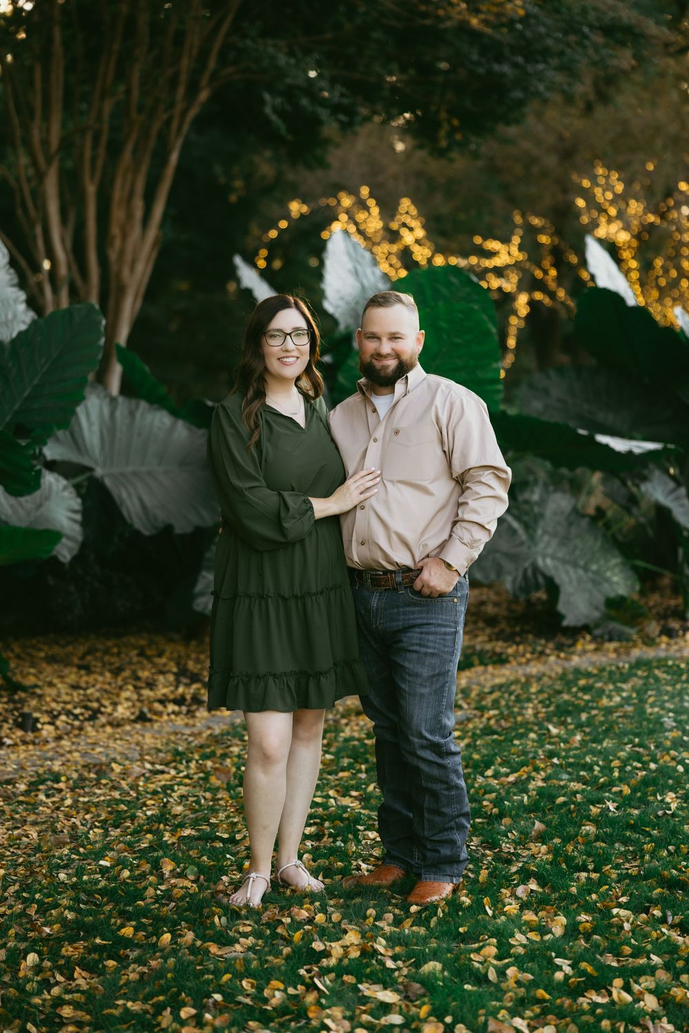 A couple poses together on fallen autumn leaves at dusk in an outdoor setting.