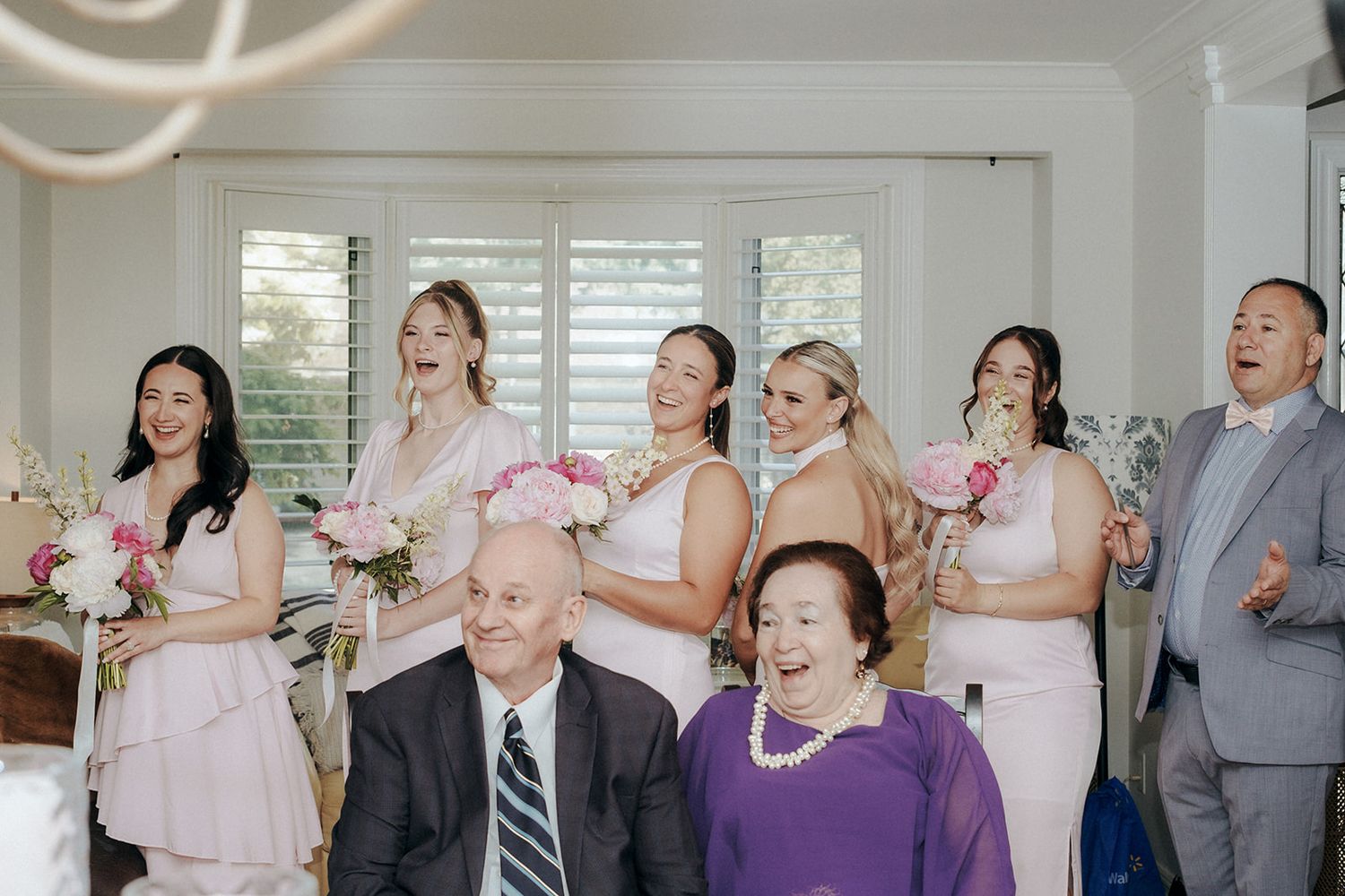 Wedding celebration in sunny room with guests wearing pink and purple formal attire.