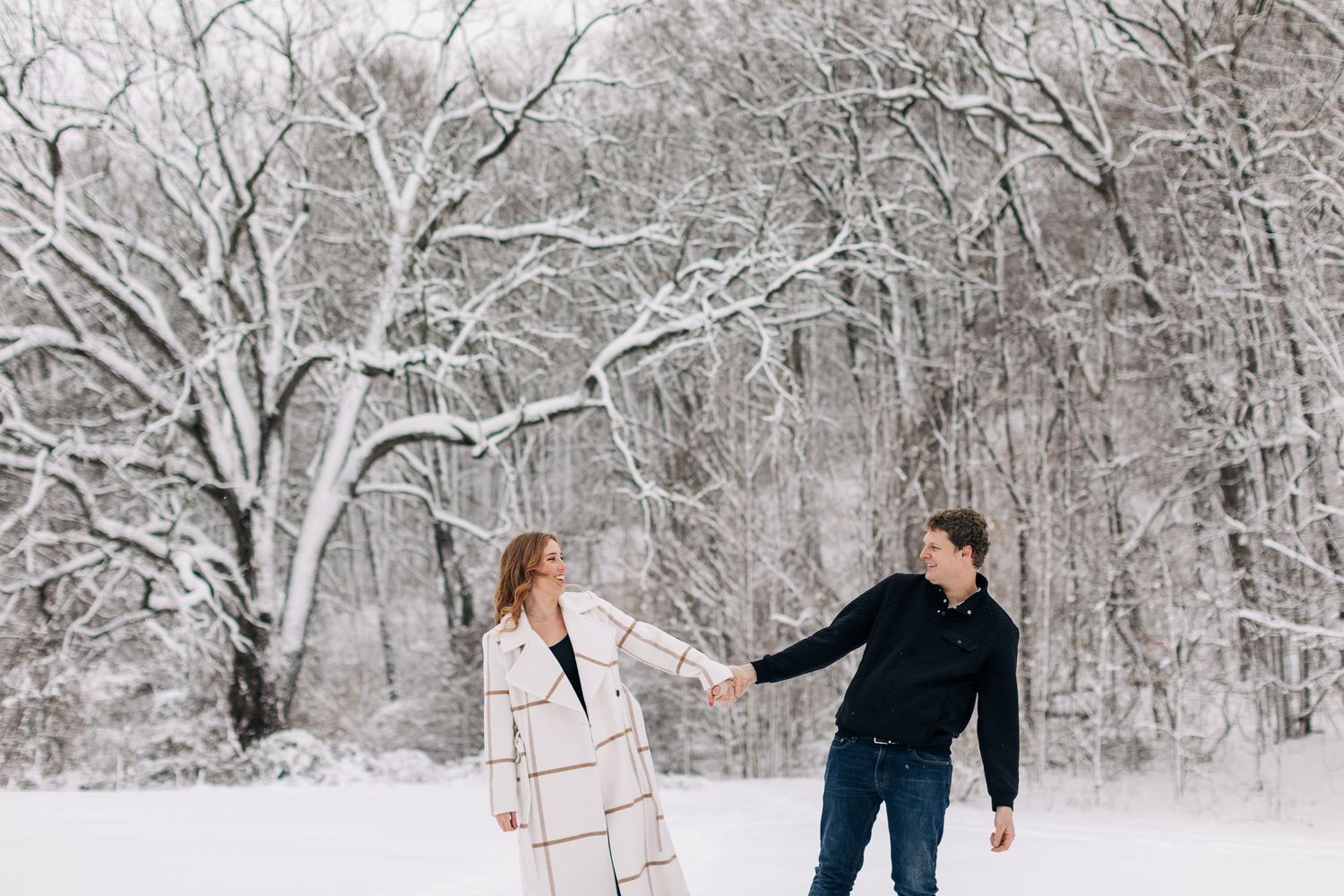 Playful couple in winter wonderland with snow-covered trees.