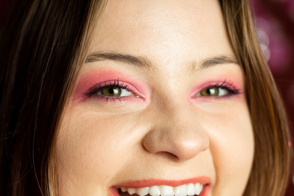 A close up photo of a person wearing bright pink eye shadowing and smiling.