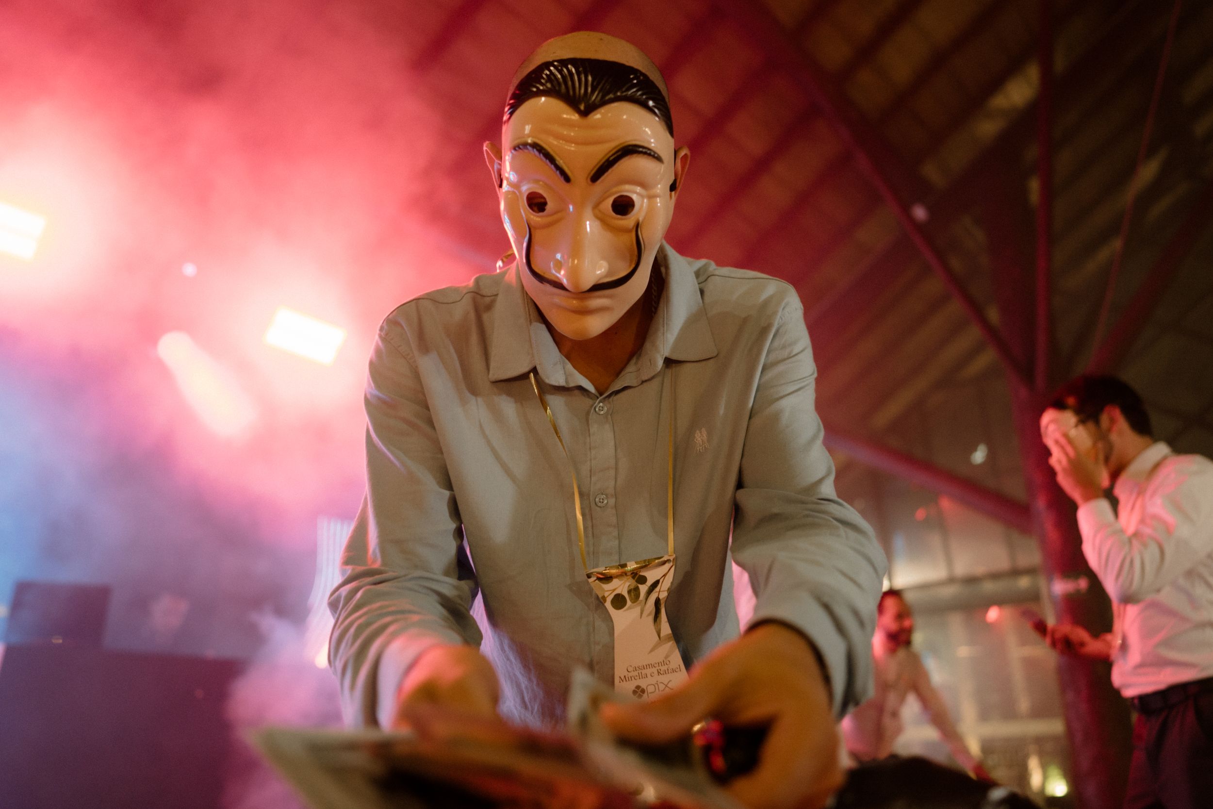 Someone wearing a Salvador Dali mask poses dramatically in moody red lighting.