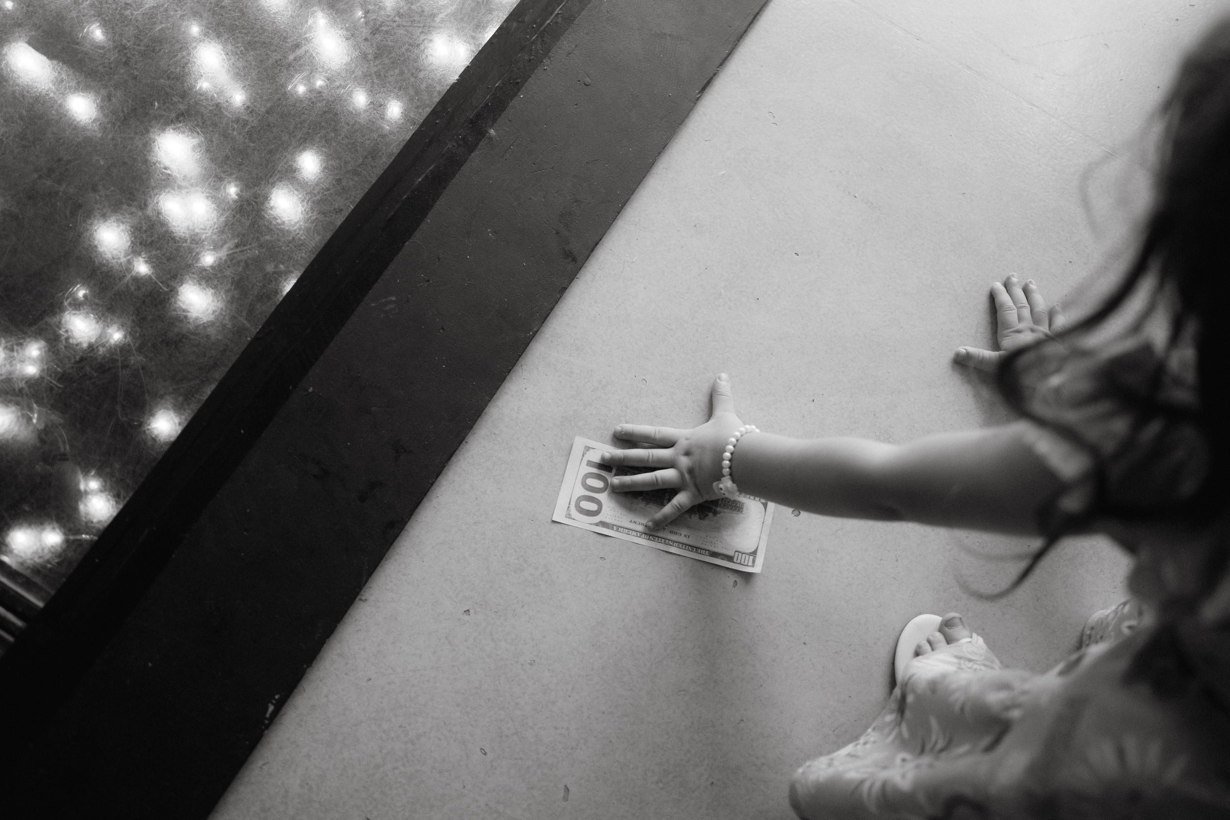 Black and white photo of hands reaching for money on a table under twinkling lights.
