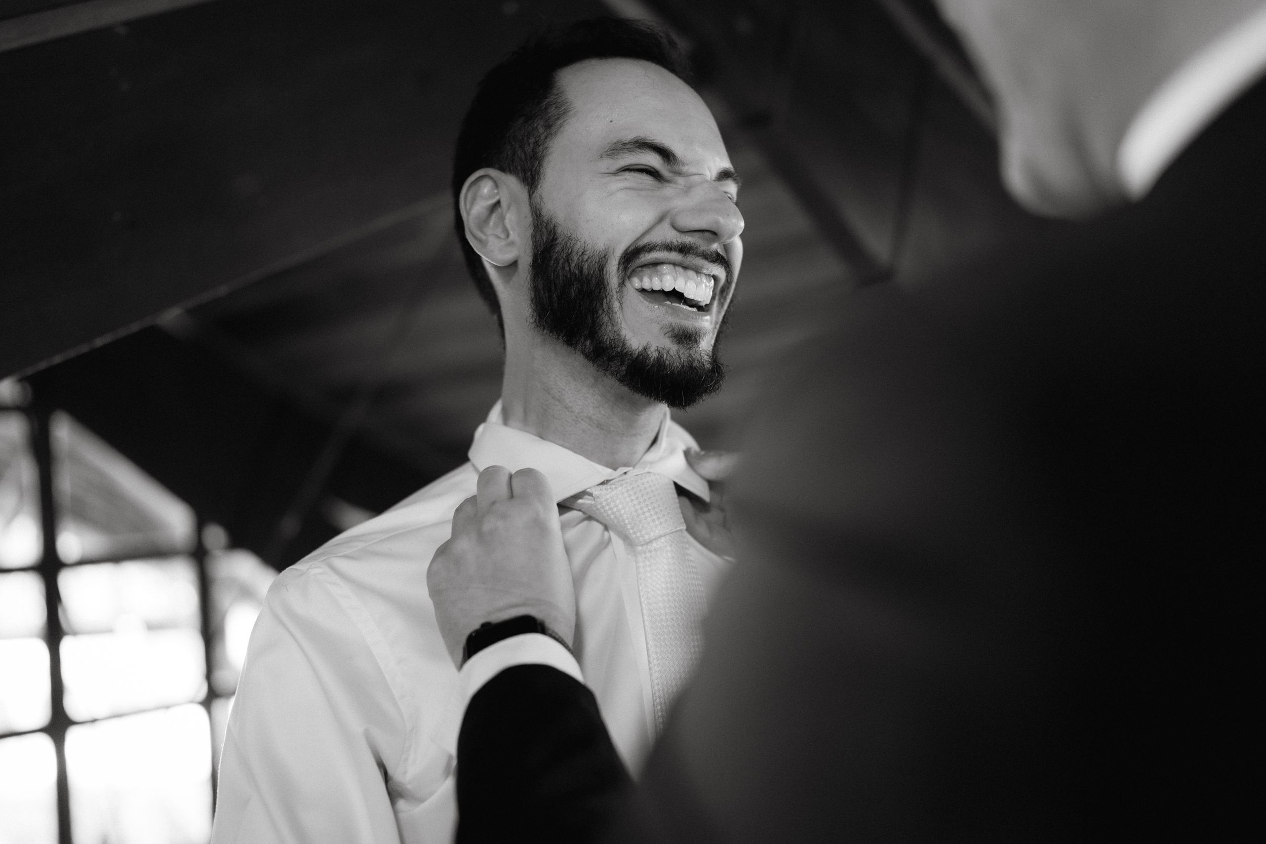 Black and white candid shot capturing joyful laughter during wedding preparations.