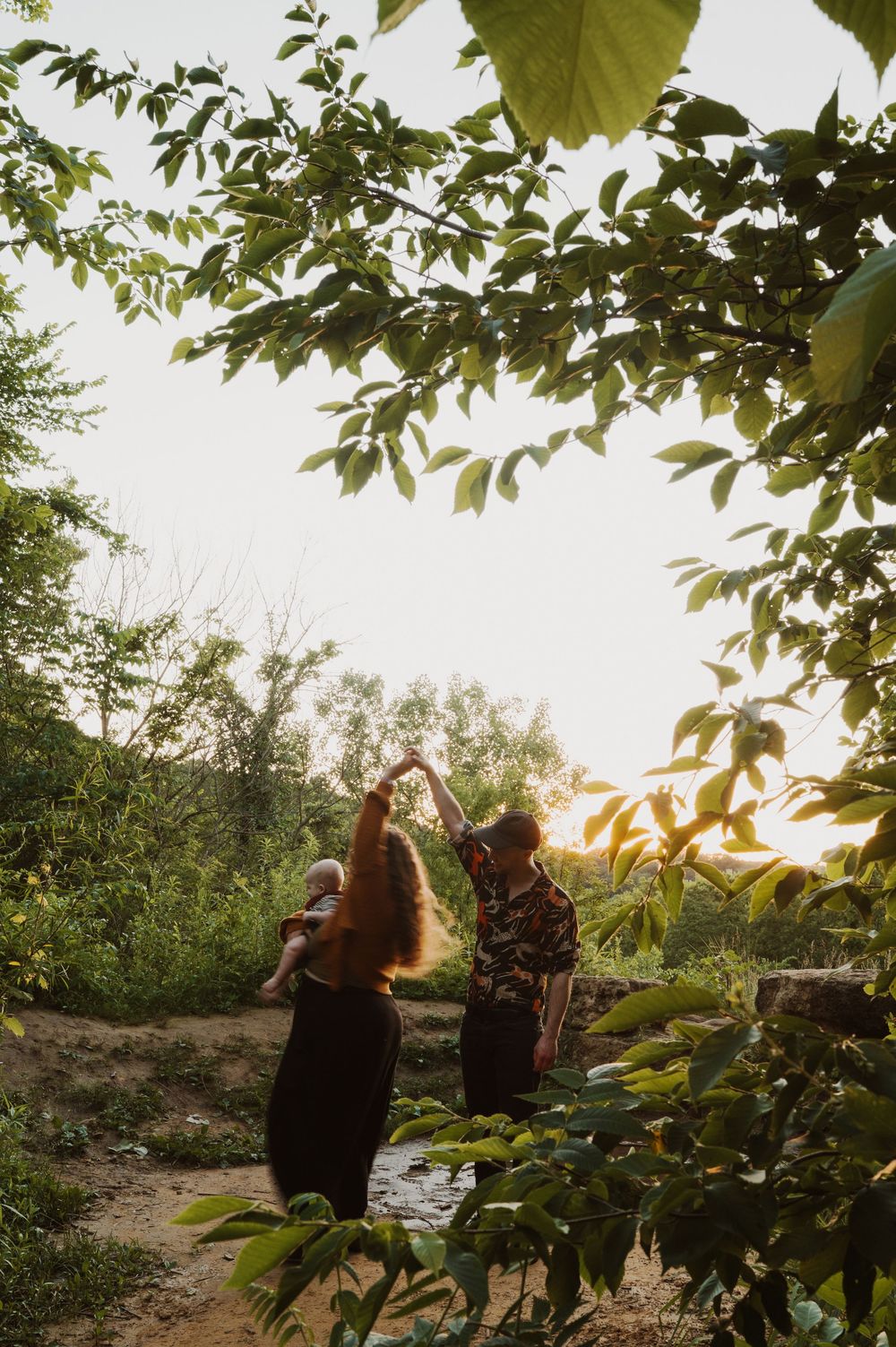 Two people dancing together at sunset in a lush green forest clearing, with warm golden light filtering through the trees.