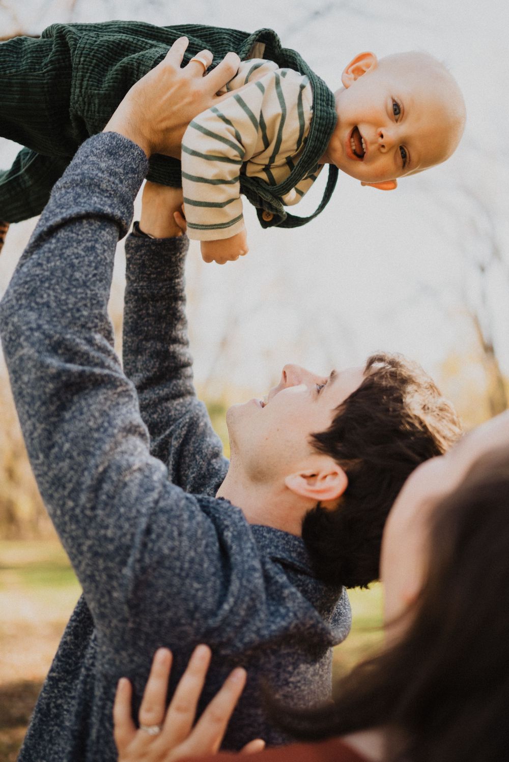 Parent lifting small child playfully against autumn outdoor background.