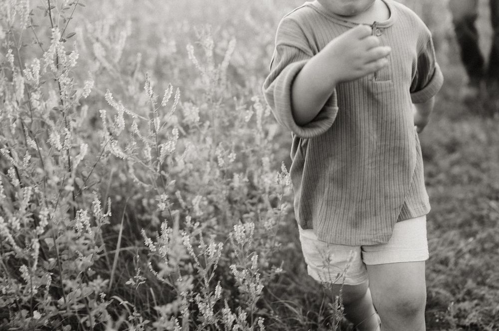 Black and white photo of a young child standing near wildflowers in a field.