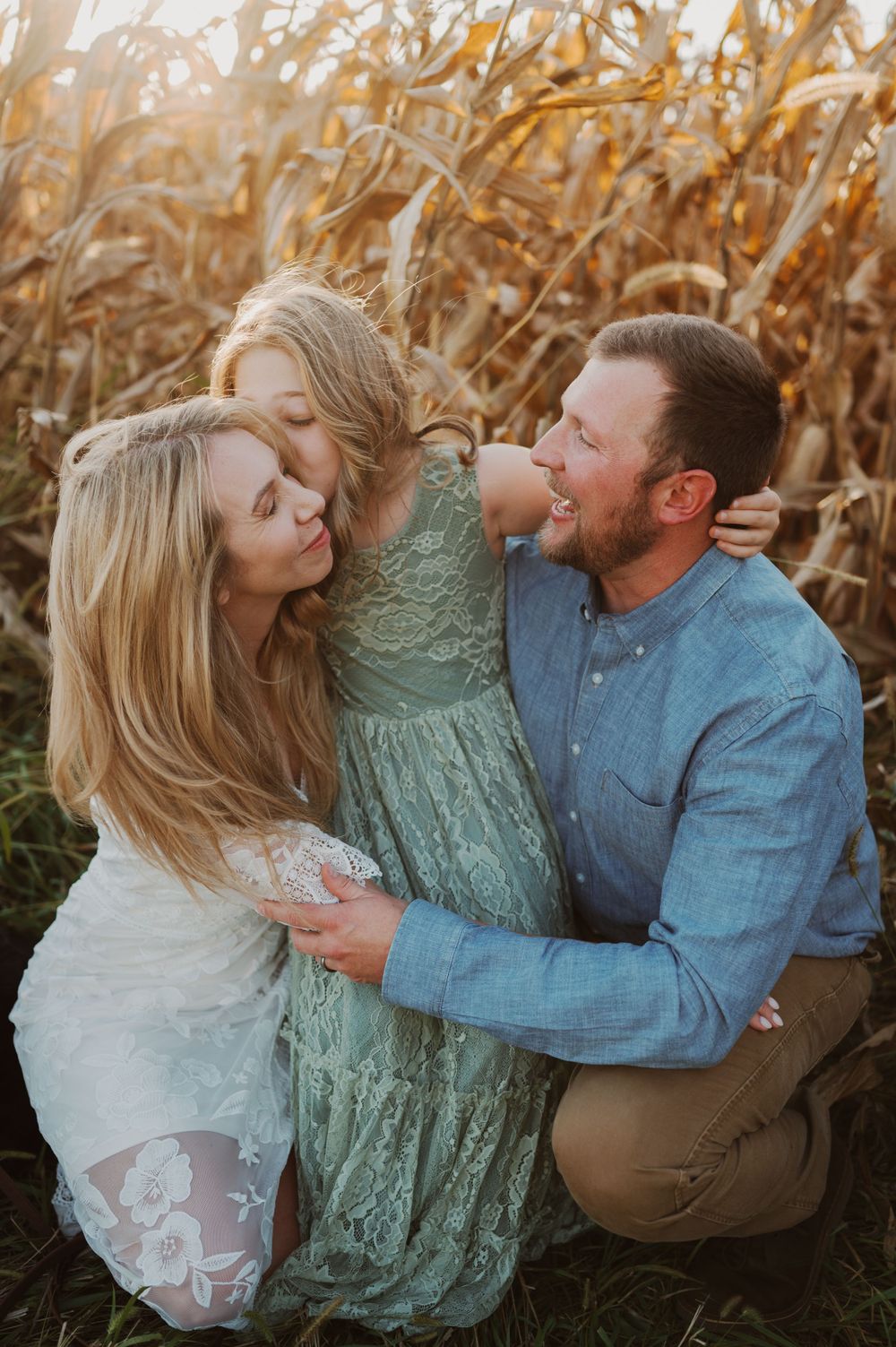 A loving couple embraces while sitting in a golden cornfield during sunset.