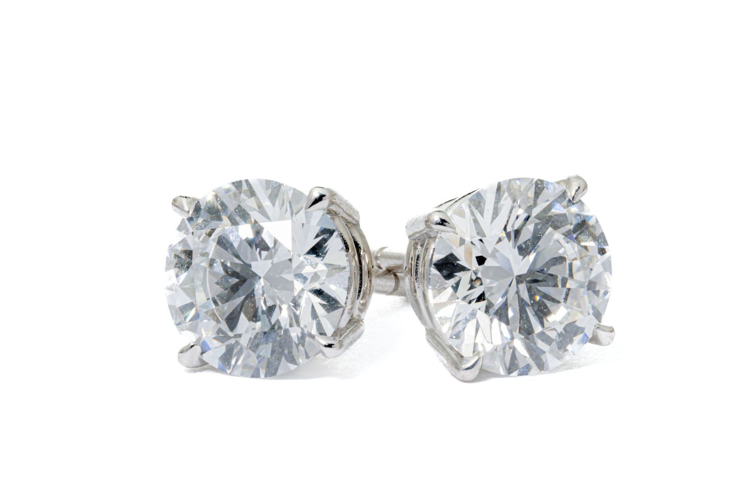 A pair of round brilliant diamond stud earrings set in silver or white gold prongs on a white background.