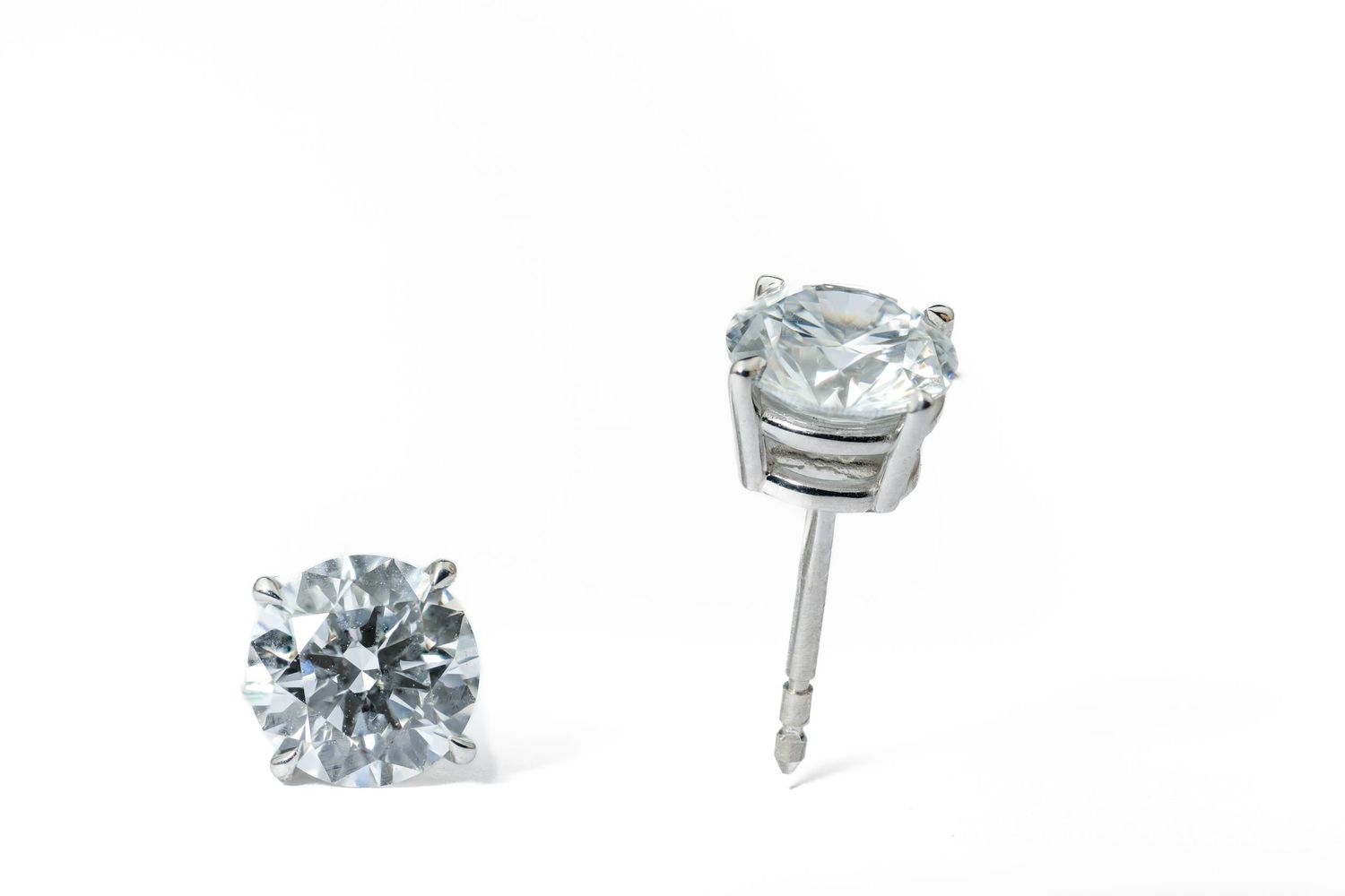 Close-up view of round brilliant diamond stud earrings with prong settings in white metal.