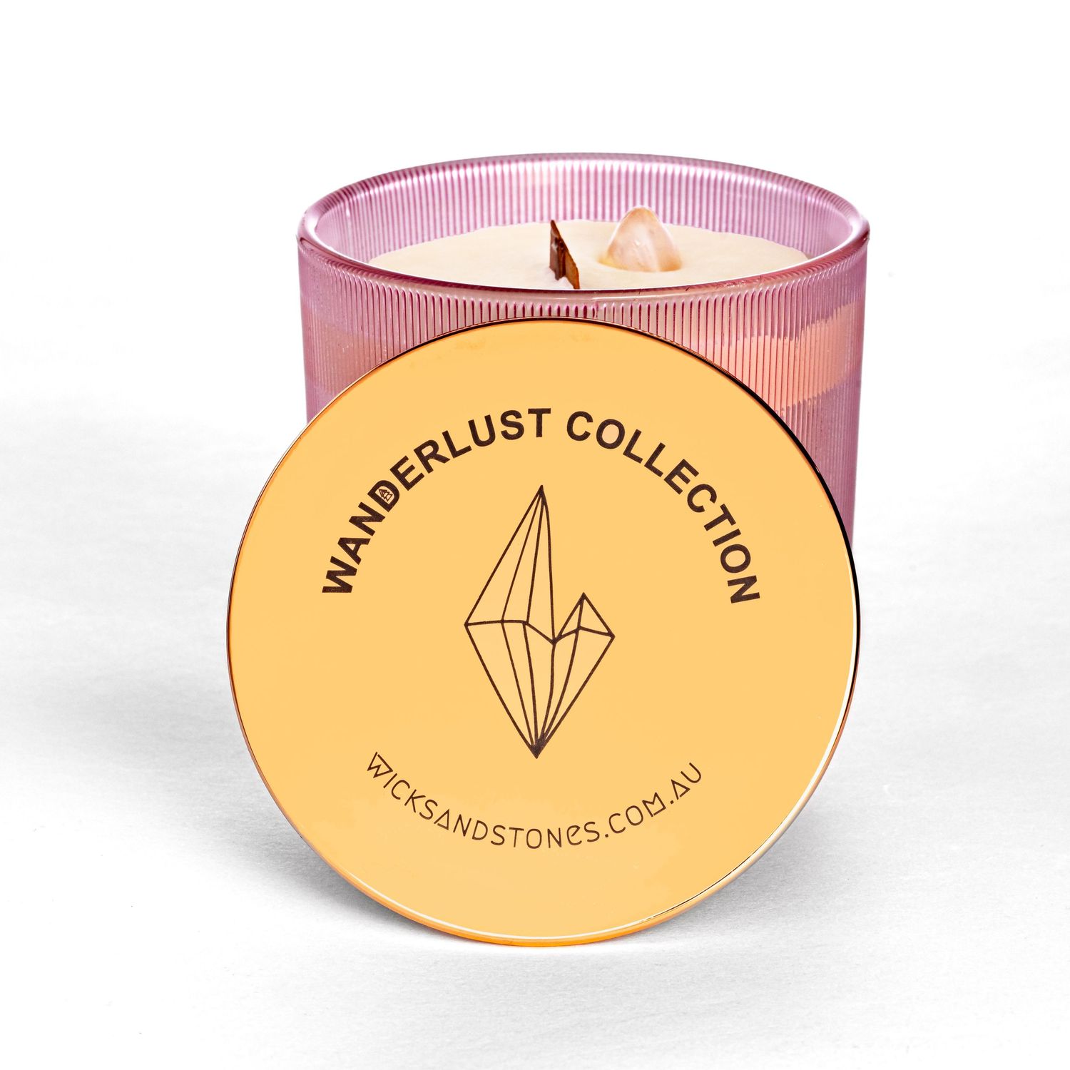 Pink glass candle with gold lid from Wanderlust Collection featuring crystal design glows warmly with lit double wick.