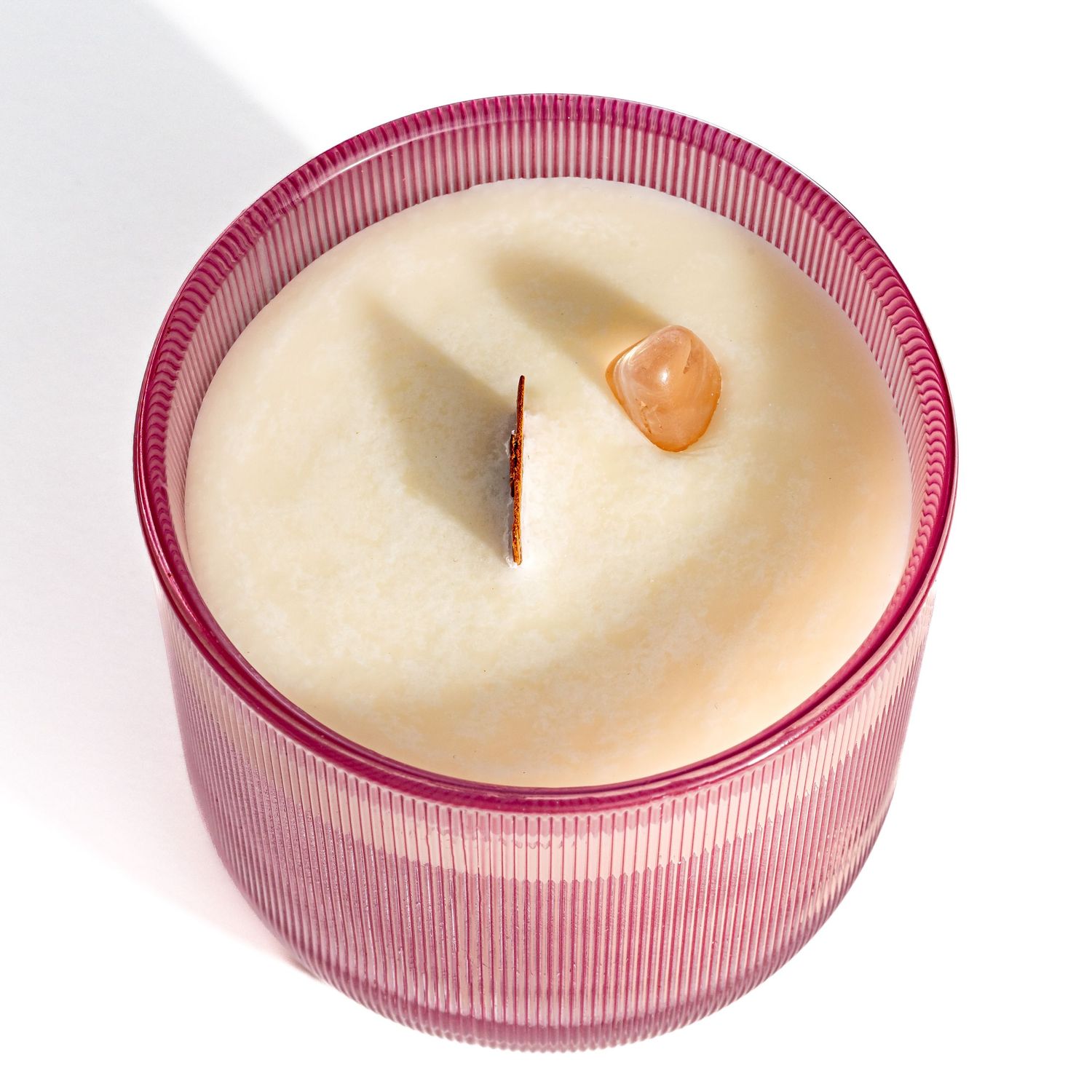 Pink ribbed glass candle holder with white wax inside and a single wooden wick on top.