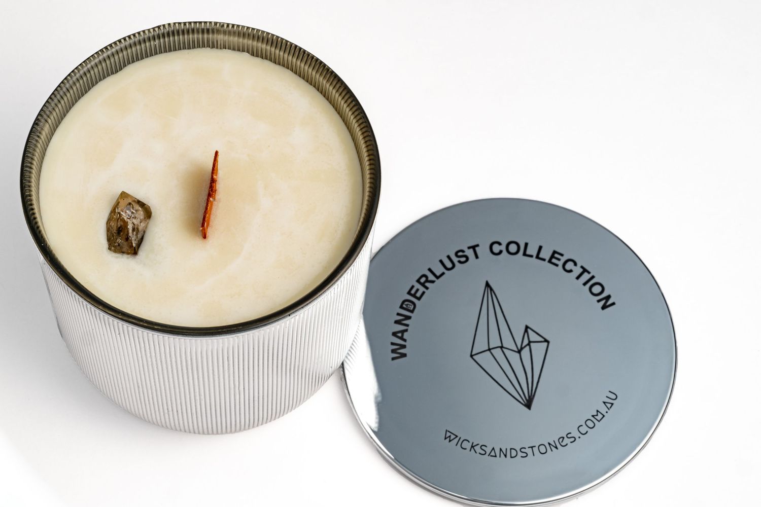 A white wooden wick candle in a ribbed container with a minimalist gray circular lid featuring crystal artwork.
