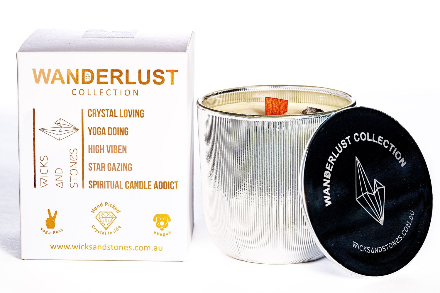 A white and gold Wanderlust Collection candle in a textured glass jar with black lid and product packaging.
