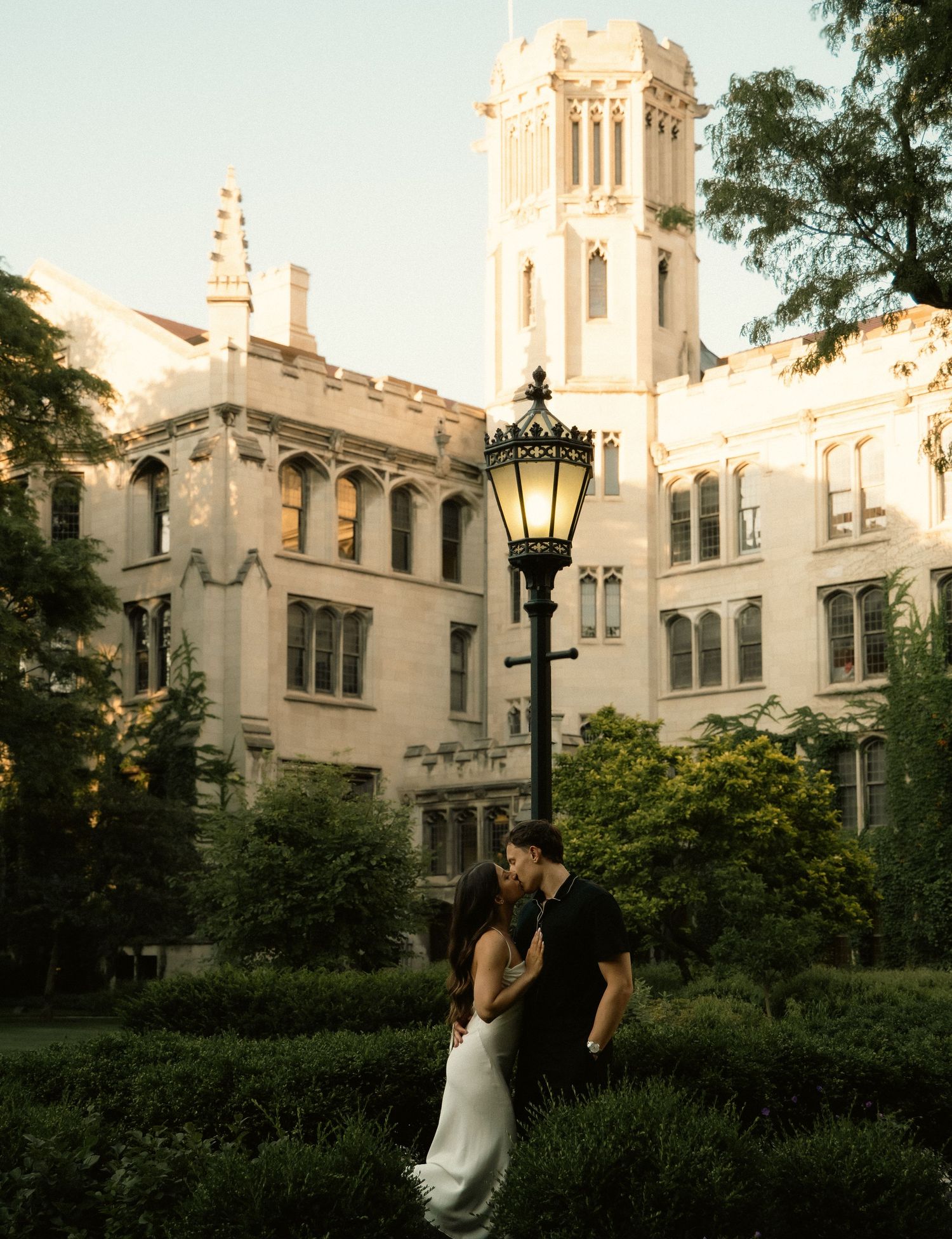 A couple embraces near a gothic university tower at golden hour.