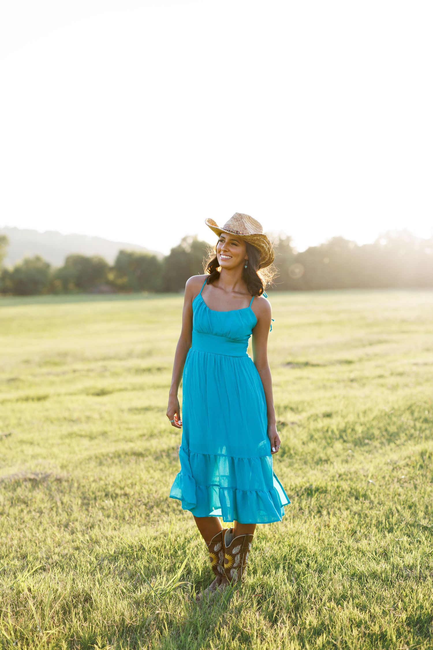 Person in flowing turquoise dress dancing in sunlit field at golden hour.