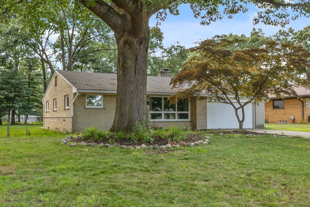 Ranch-style home surrounded by large mature trees, green lawn, and attached two-car garage.