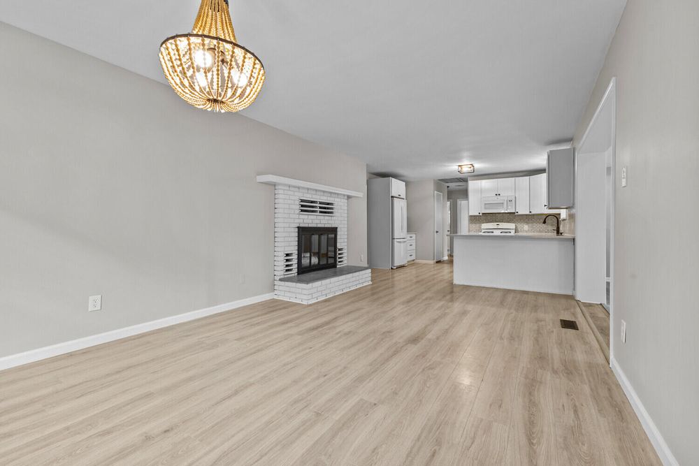 Bright living room featuring a white brick fireplace, light wood floors, and elegant chandelier.