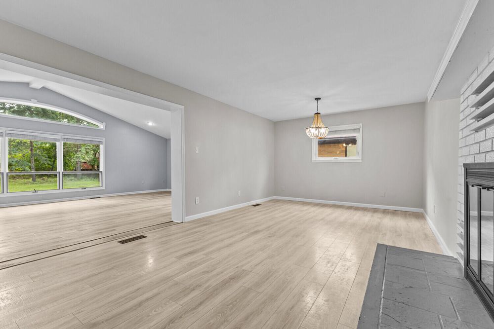 Spacious open living area with light hardwood floors, brick fireplace, and view into adjacent room.