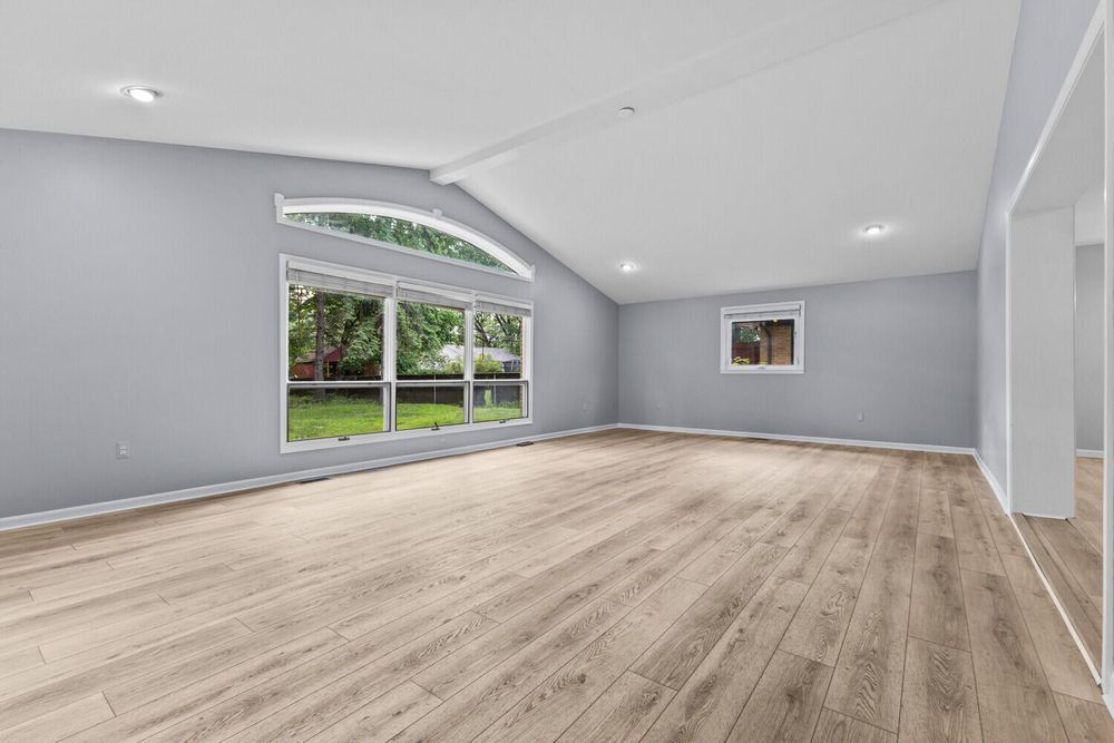 Vaulted ceiling room with large arched windows, recessed lighting, and light hardwood flooring.