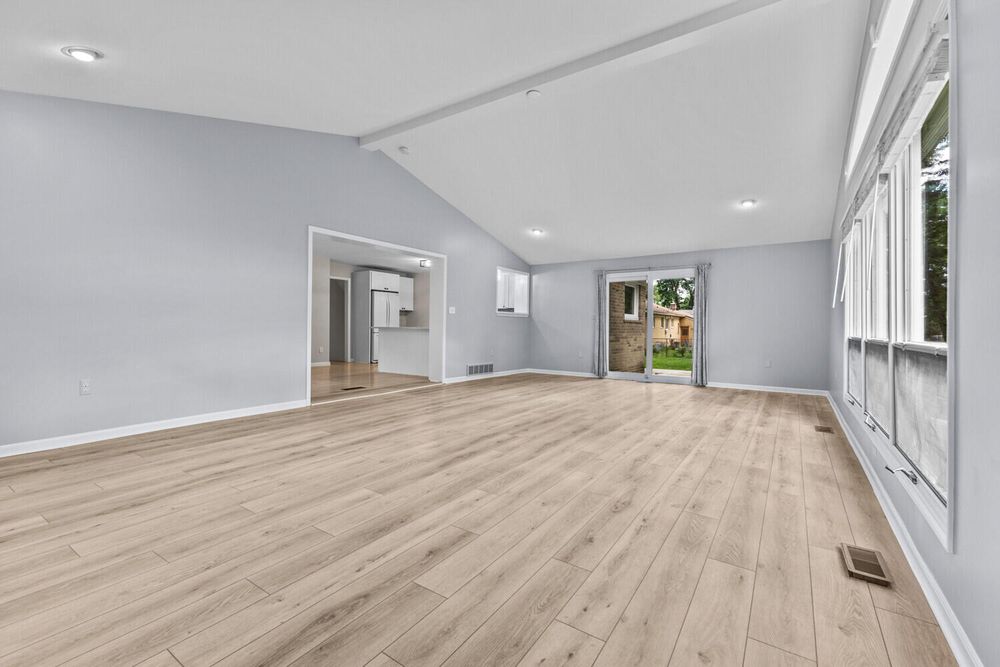 Open living space with vaulted ceilings, light hardwood floors, and large windows with natural light.