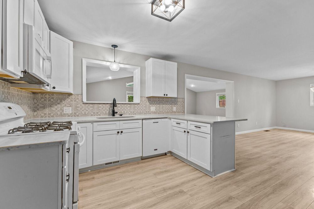 White kitchen with peninsula, subway tile backsplash, pendant lighting, and light hardwood floors.