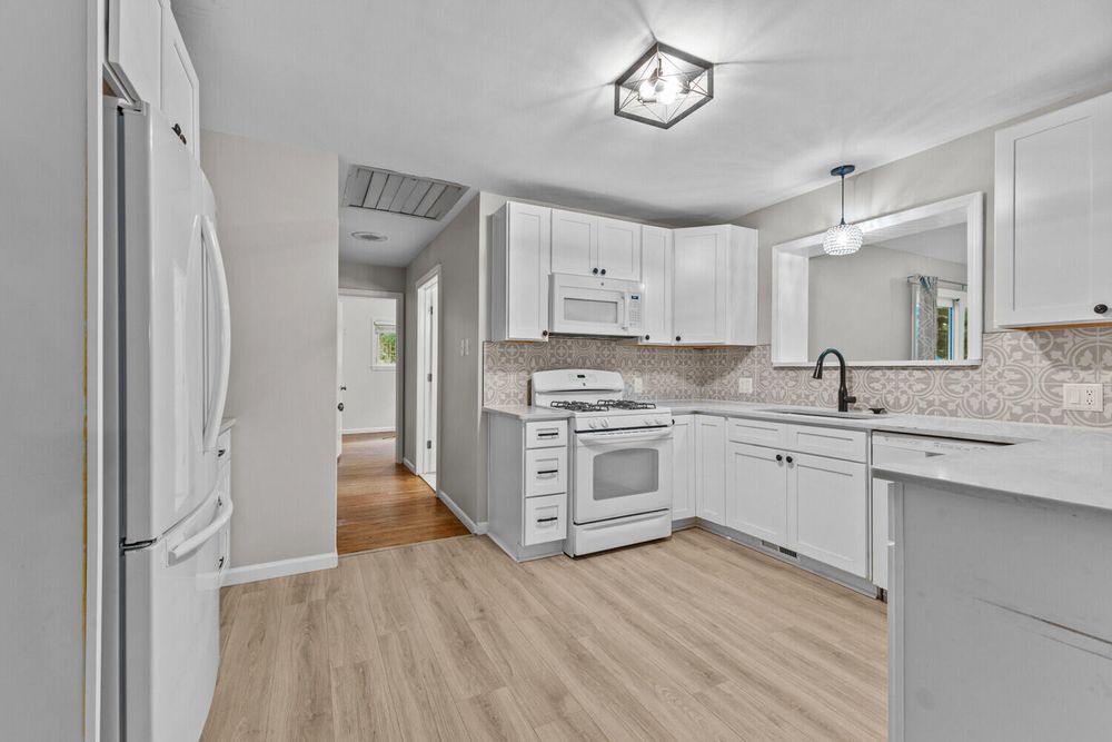 Bright white kitchen featuring white appliances, subway tile backsplash, and light hardwood floors.