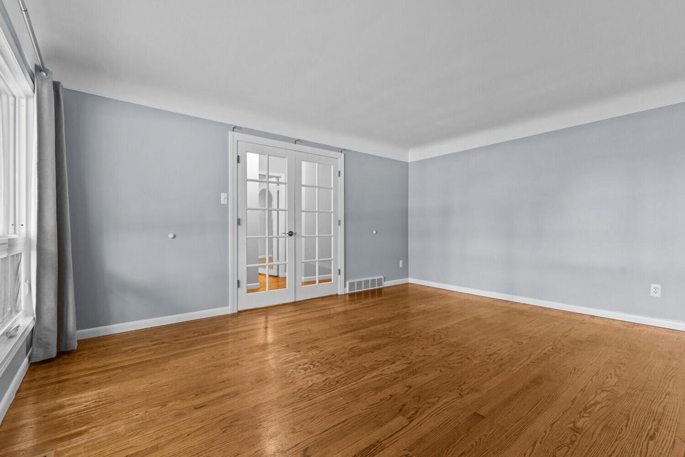 Empty living room with hardwood floors, crown molding, French doors, and light blue-gray walls.