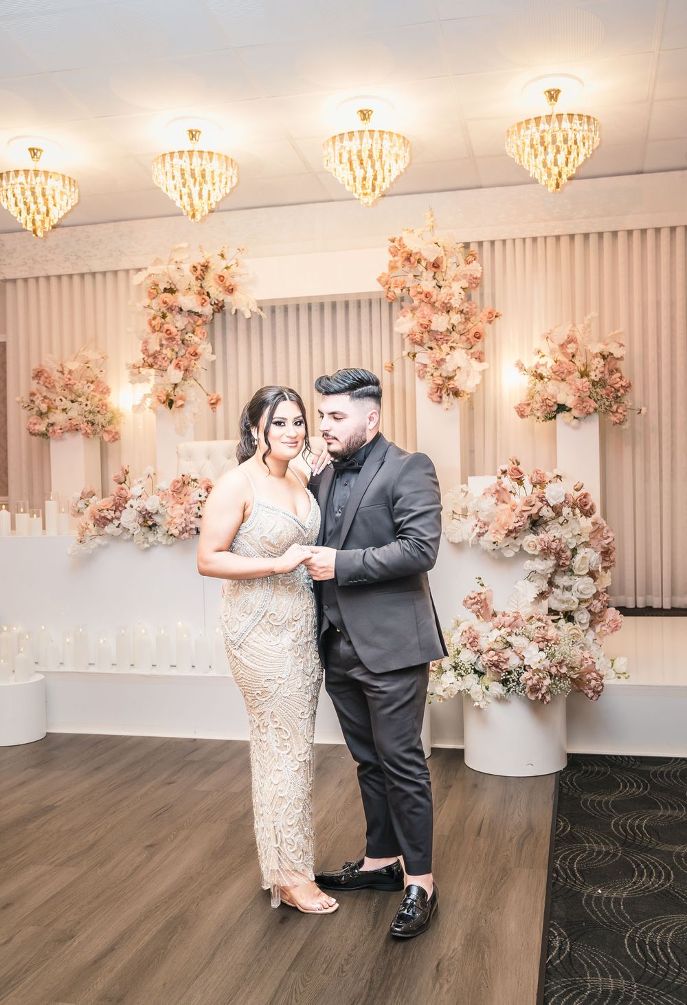 A couple dances in an elegant reception room with crystal chandeliers and floral arrangements.
