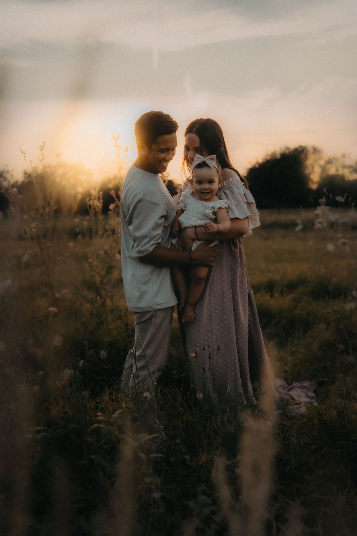 A family shares an intimate moment together in a golden sunset-lit field with tall grass and wildflowers.