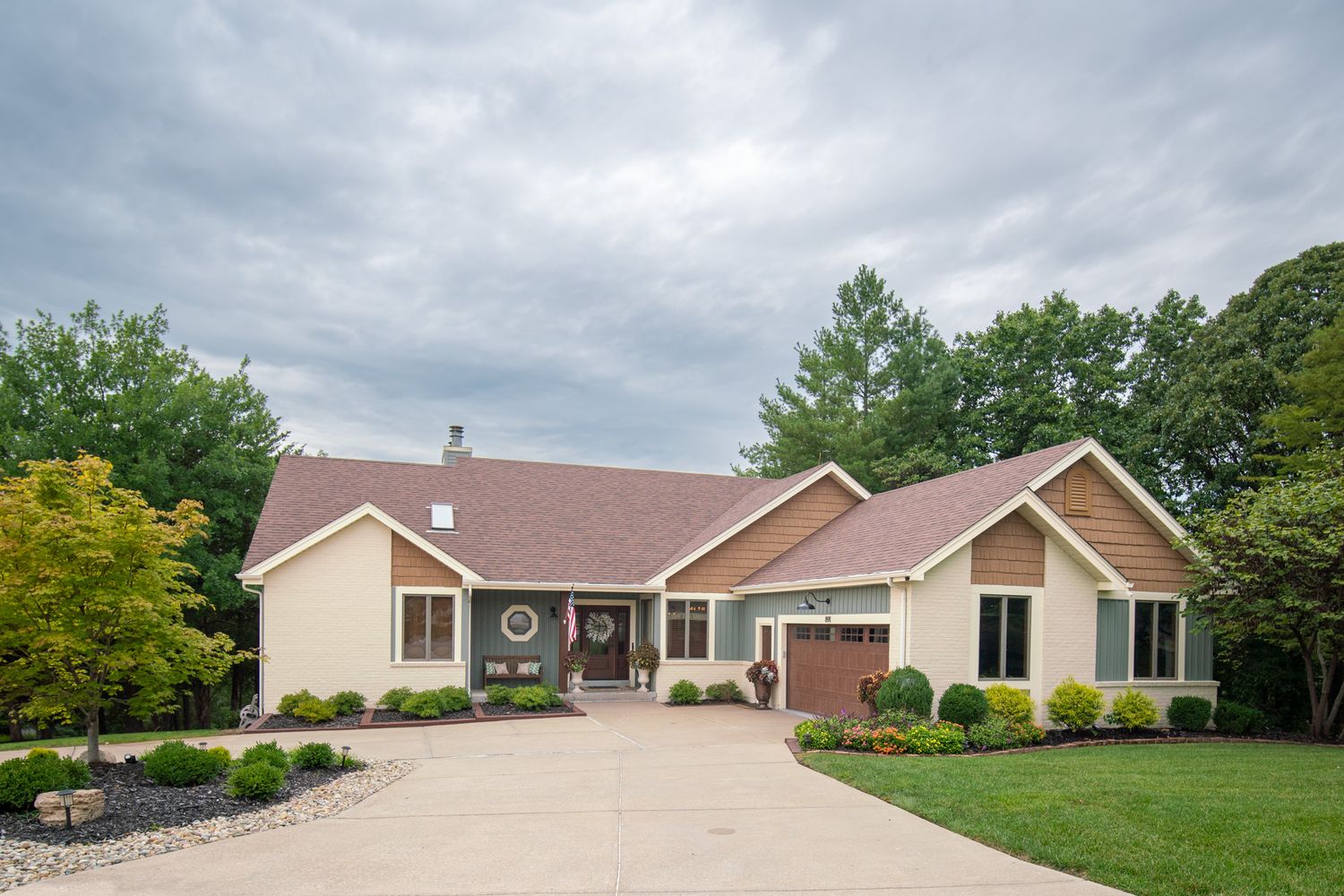 Modern ranch-style home with attached garage and manicured landscaping under cloudy skies.