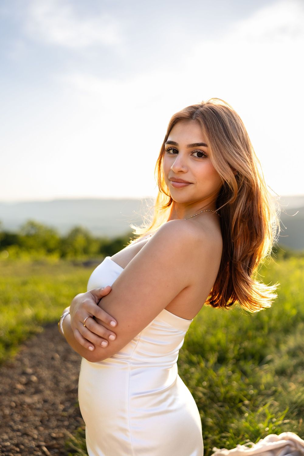 Portrait photo of someone in a white dress standing in a grassy field during golden hour with long brown hair.