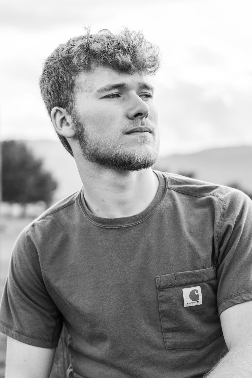 Black and white portrait of a young man looking into the distance wearing a casual t-shirt with pocket.