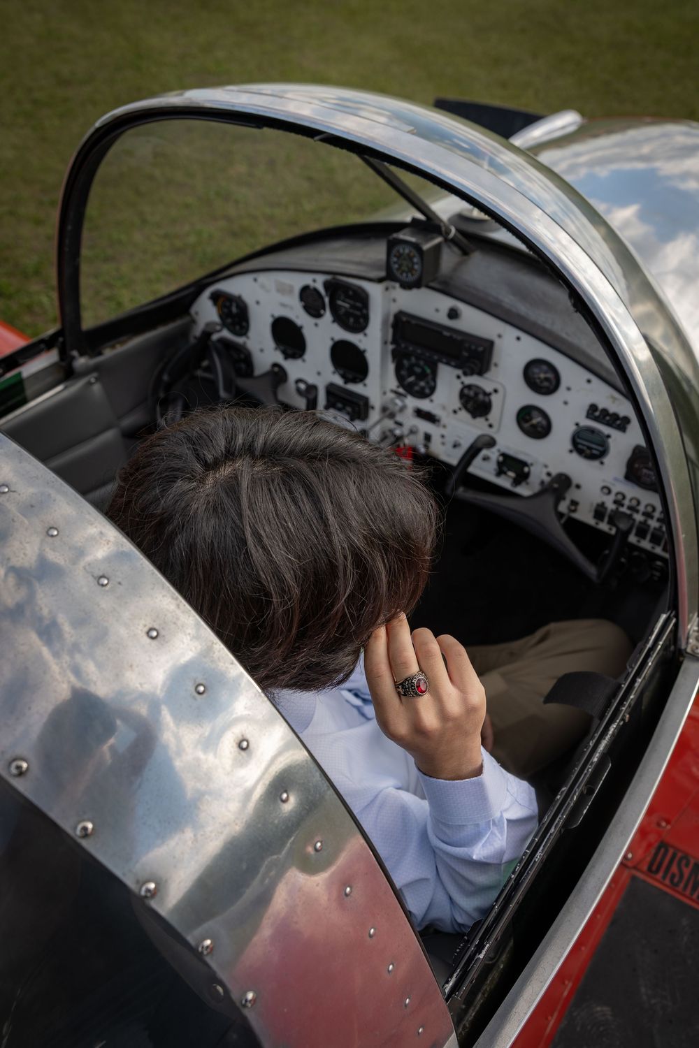 Person sitting in a small aircraft cockpit viewed from above, examining flight instruments and controls on the dashboard.