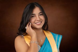Portrait against brown backdrop showing bright yellow and turquoise traditional attire with jewelry and a warm smile.