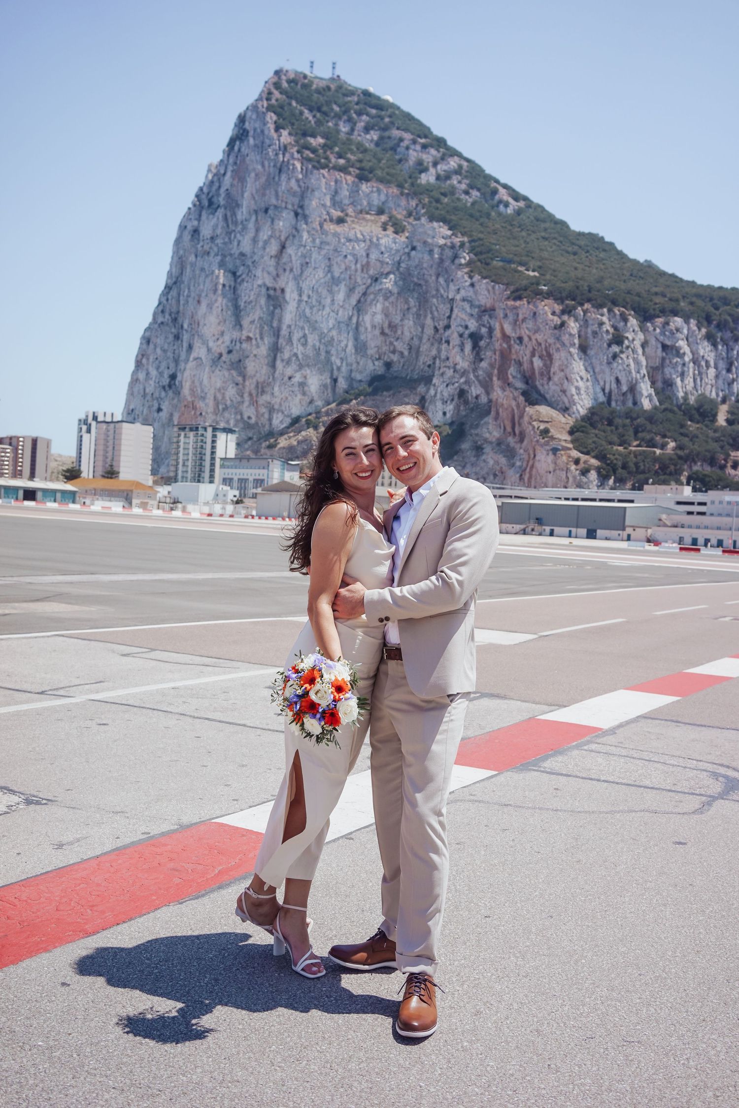 Bride holds flowers while in embrace with groom on the runway at Gibraltar Airport
