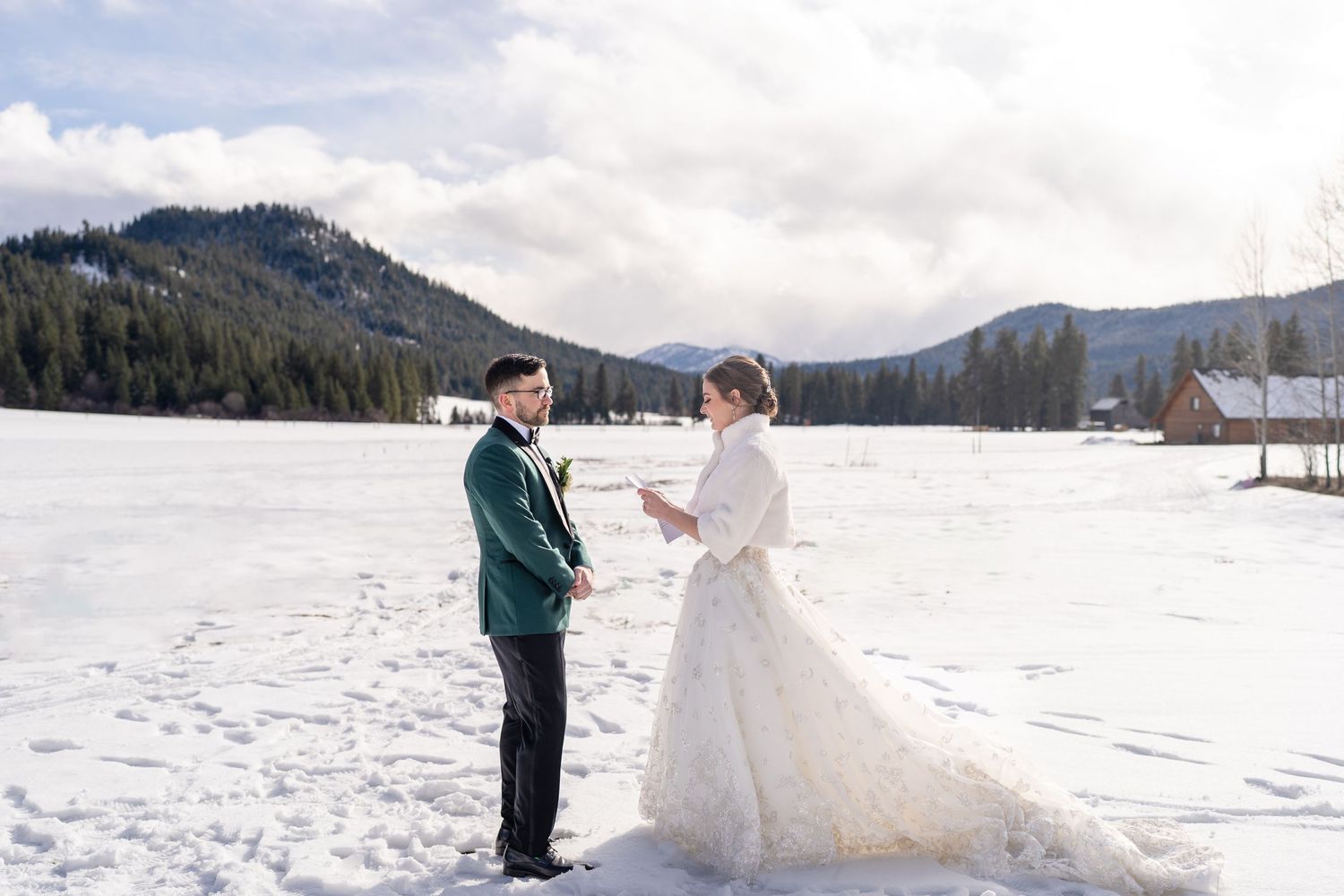 A winter wedding scene with a couple standing in the snow against a mountain landscape.