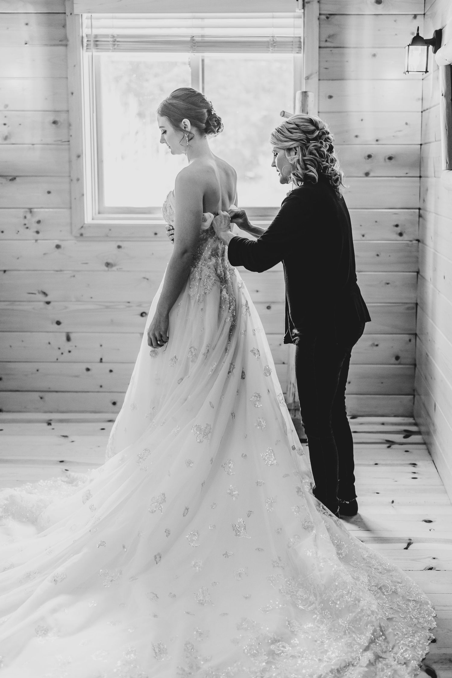 A black and white photo of wedding dress preparations in a rustic cabin setting.