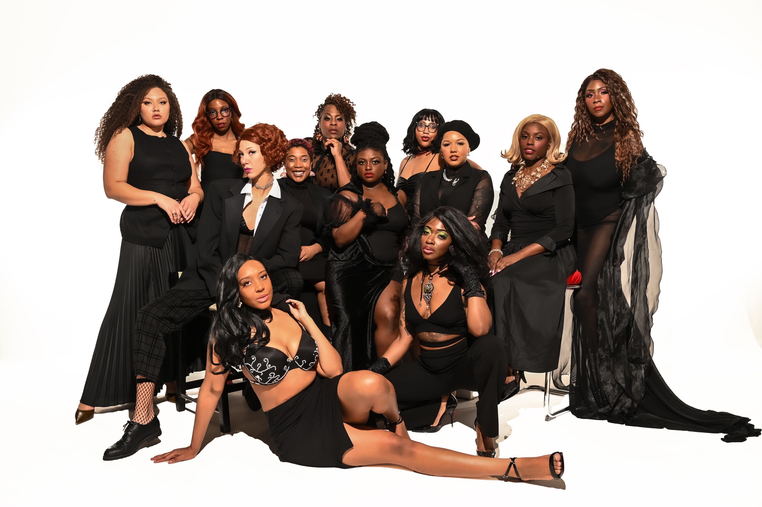 A group of people dressed in black outfits poses together for a stylish group portrait against a white background.