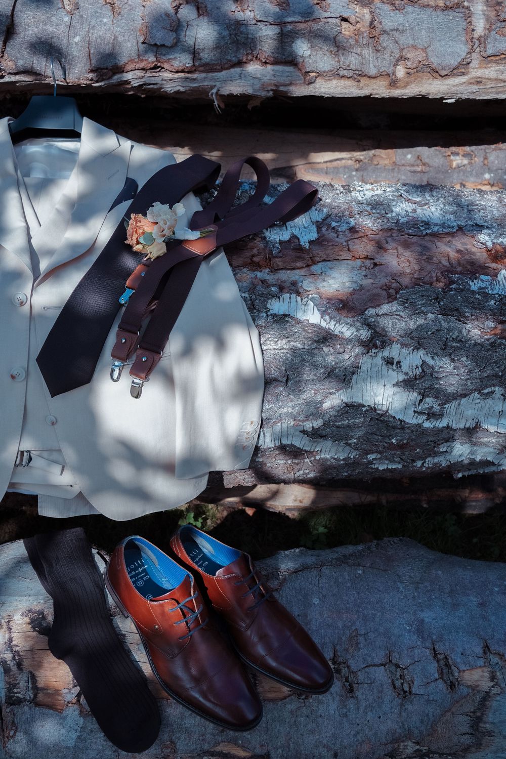 A white dress shirt with tie and brown leather shoes arranged on a textured blue background with dramatic shadows.