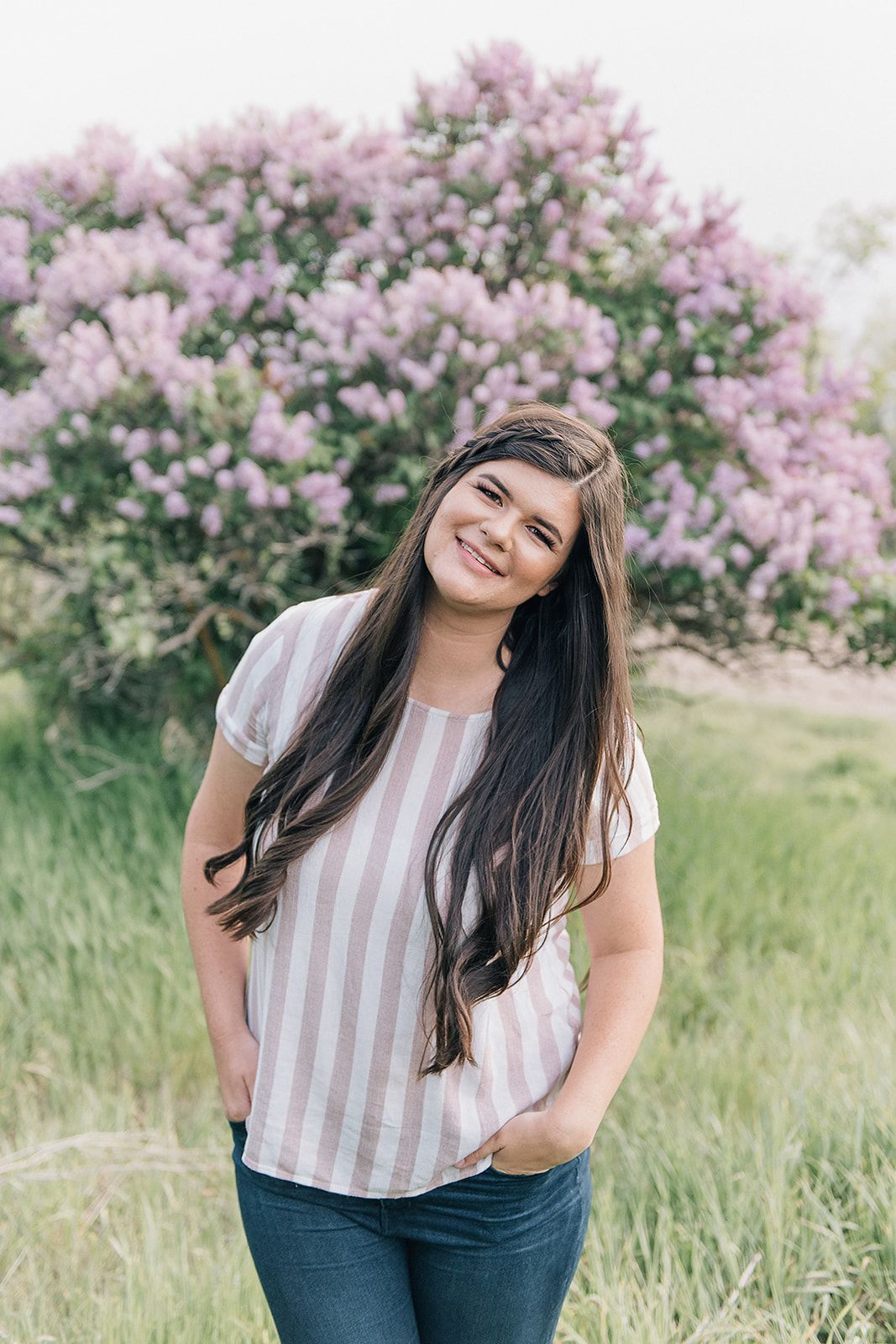 Woman in striped shirt smiling in front of blooming pink lilac bush.