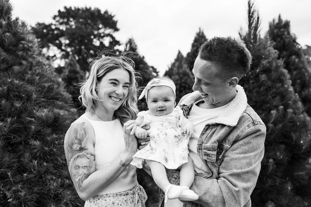 Black and white portrait of a family sharing joyful expressions in a natural outdoor setting at Christmas tree farm.