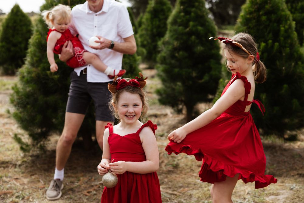Festive family photoshoot at a Christmas tree farm with red and white outfits creating joyful holiday memories.