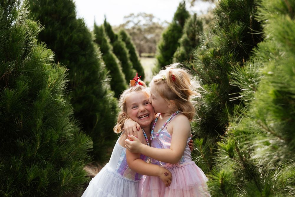 Children playing together among evergreen trees in matching tulle dresses.