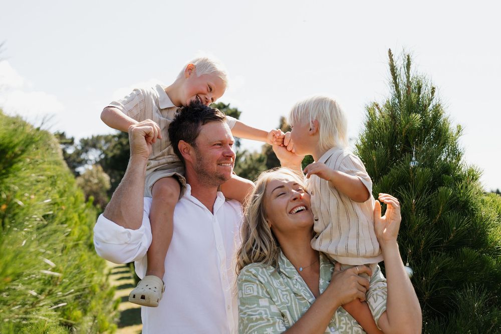 Happy family moments captured outdoors among evergreen trees during a sunny day at Christmas tree farm.