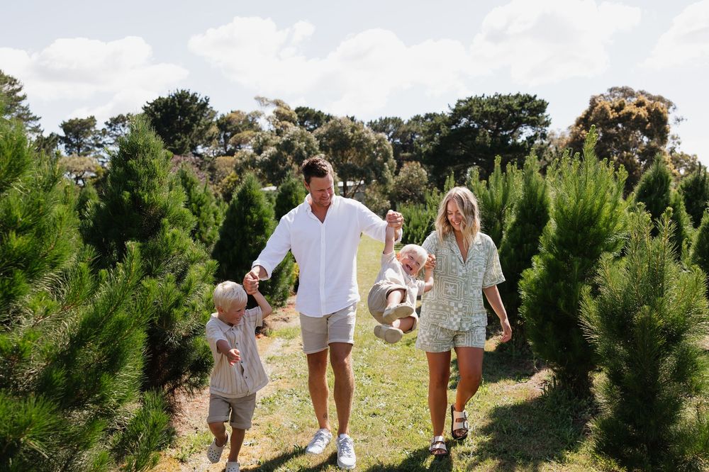 Family walking together through rows of evergreen trees on a bright summer day at Christmas tree farm.