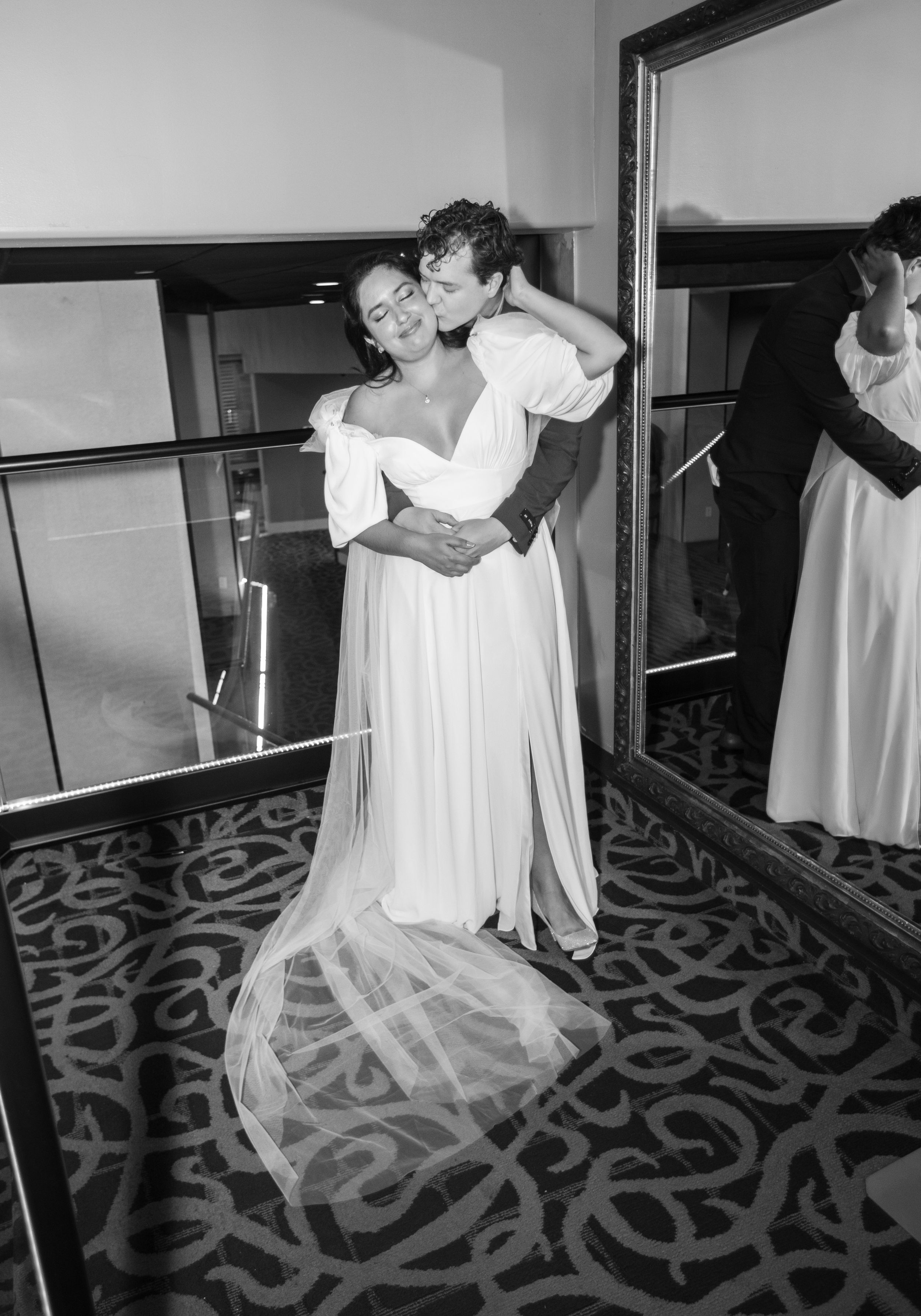 A tender embrace between figures in white attire reflected in a mirror.