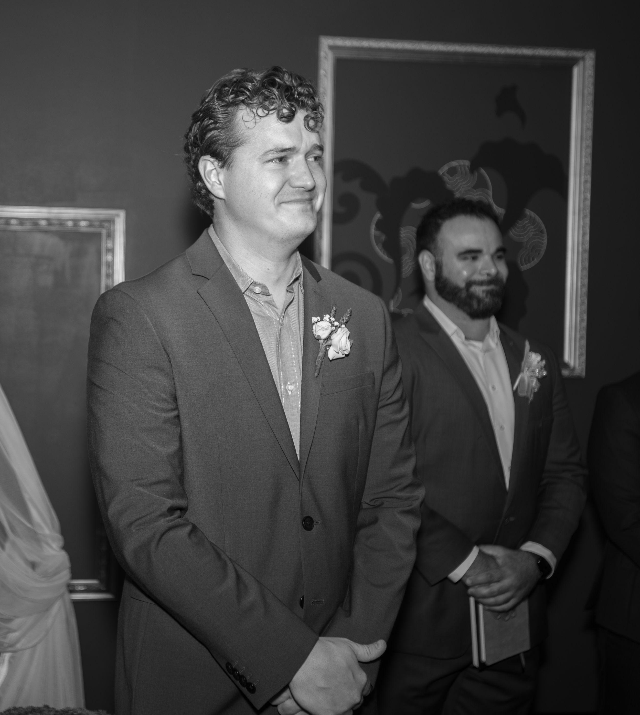 A groom wearing a grey suit and floral boutonniere stands in anticipation.
